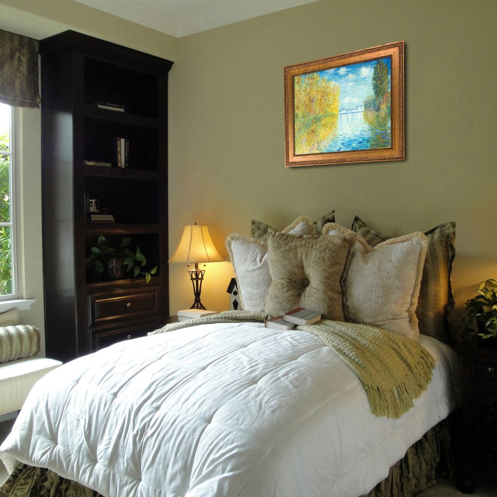 Framed autumn landscape painting hanging on a green wall above a bed in a cozy bedroom